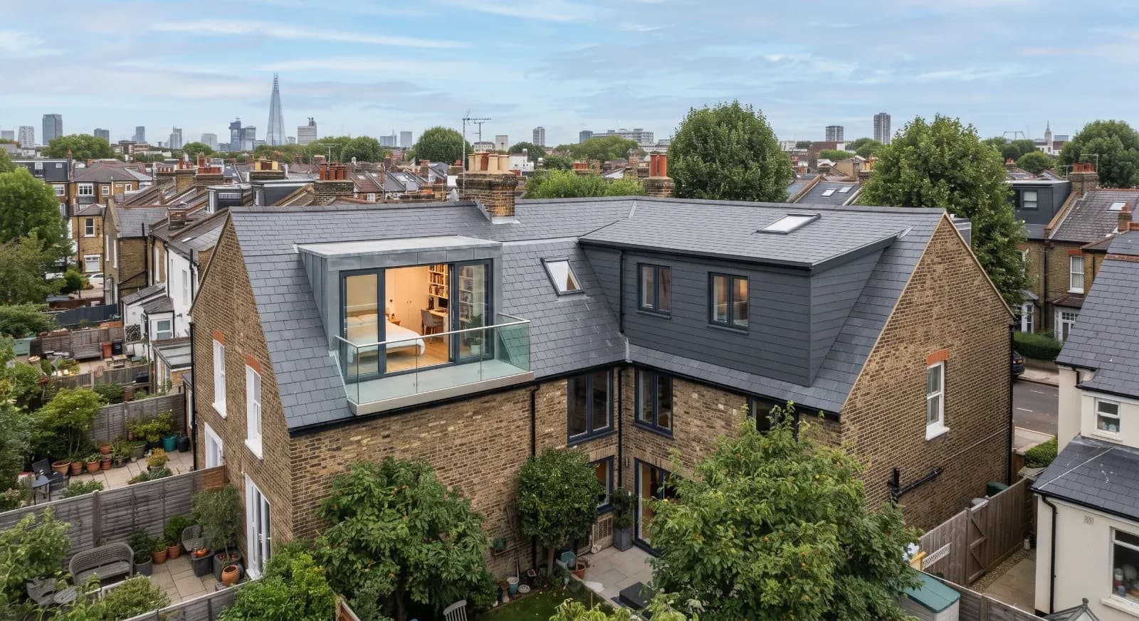 Brick townhouse with modern loft conversion featuring rear dormer extension, flat roof, and glass balcony overlooking Lo